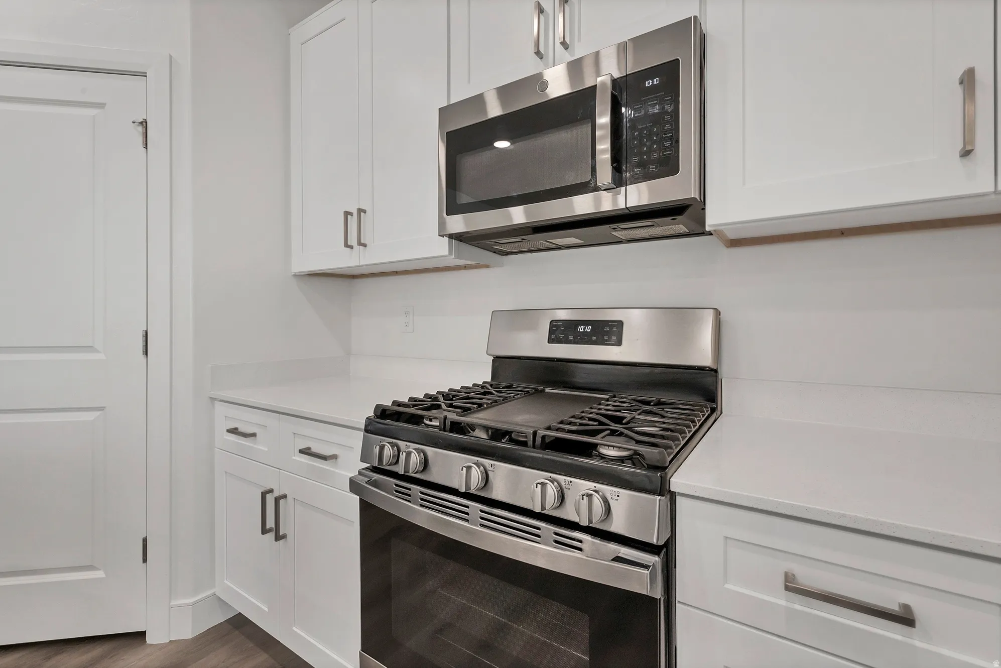 Modern kitchen featuring white shaker cabinetry, stainless steel gas range, stainless steel microwave, light-toned countertops, and wood-finish flooring