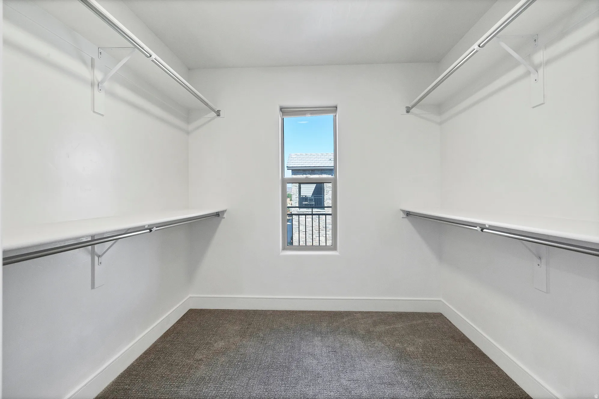 Walk-in closet featuring white walls, gray carpet flooring, and a single window with exterior building visibility