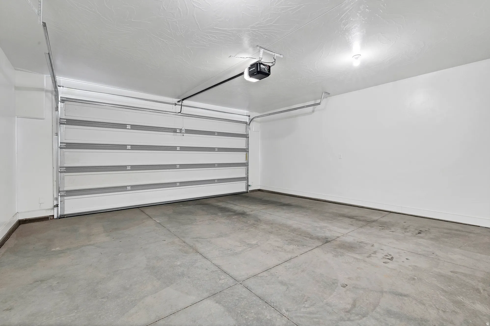 Spacious garage featuring a sectional overhead door with automatic opener, concrete flooring, and overhead lighting