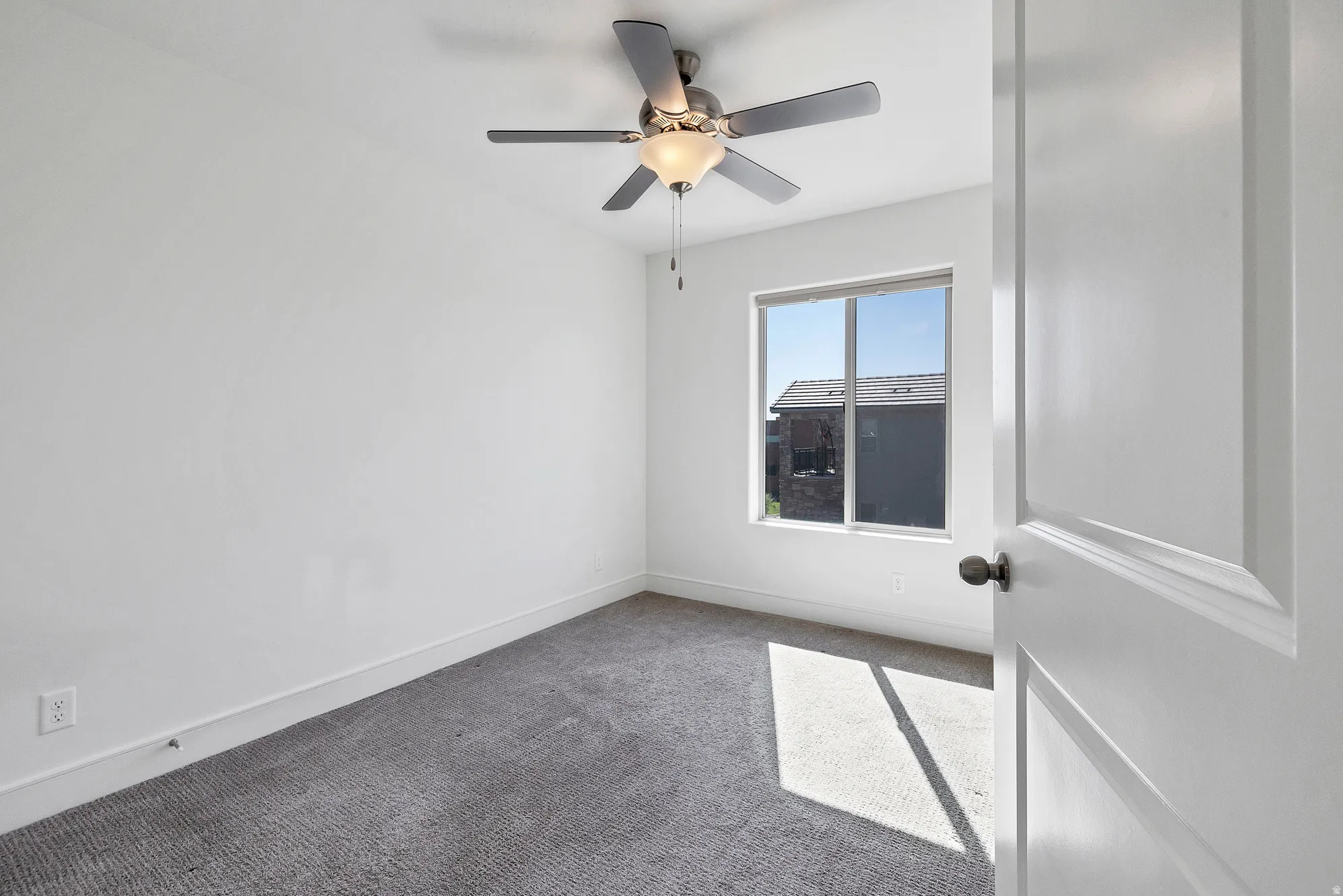 Carpeted room featuring a ceiling fan with integrated lighting, a window, and a white interior door with dark hardware