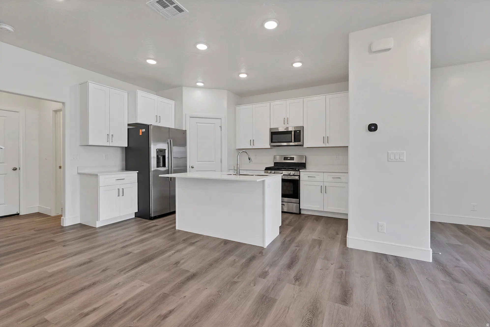 Open-concept kitchen featuring white cabinetry, stainless steel appliances, a central island, and wood-finish flooring