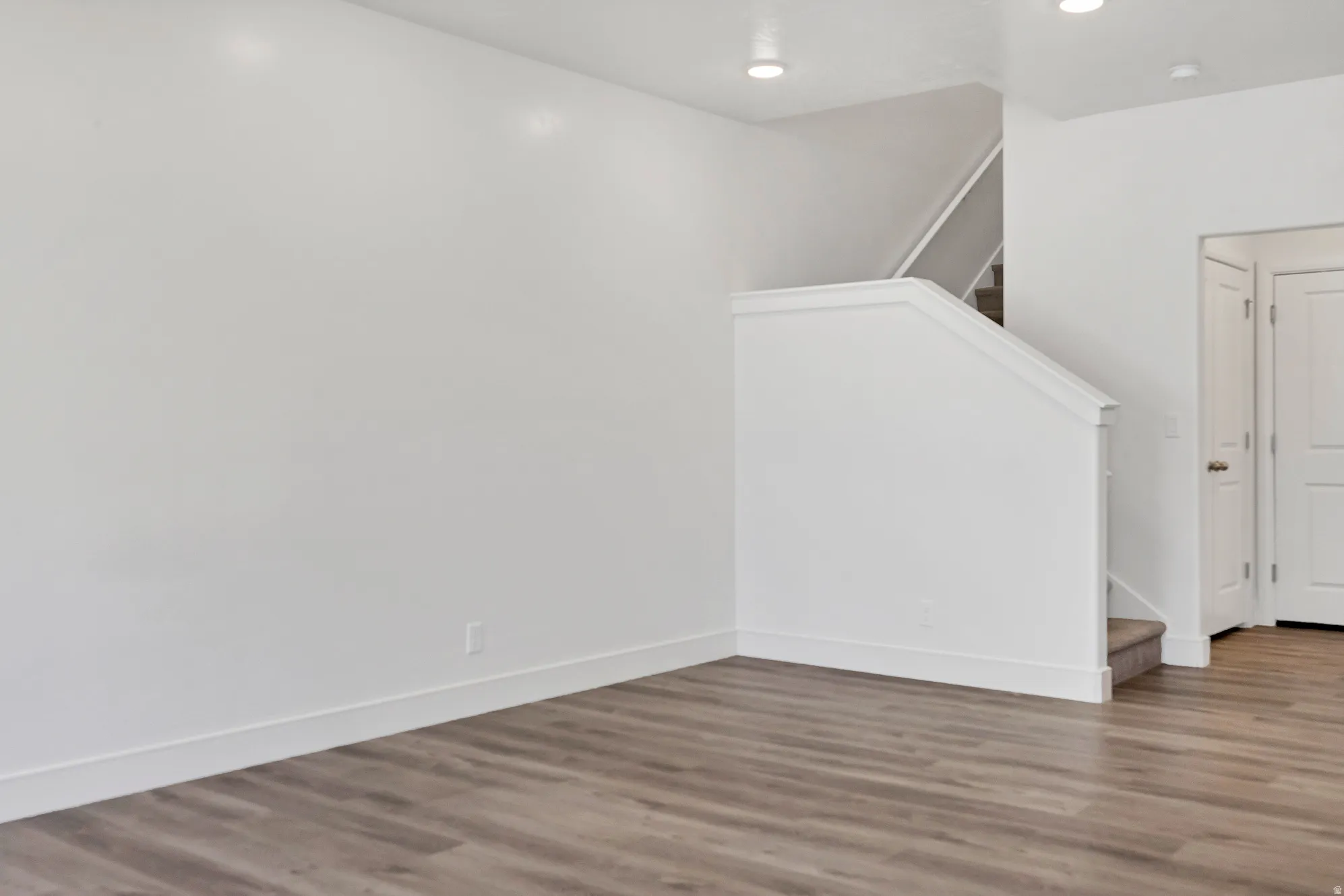 Living area featuring contemporary wood-finish flooring, recessed lighting, and a staircase with white balustrade and carpeted treads