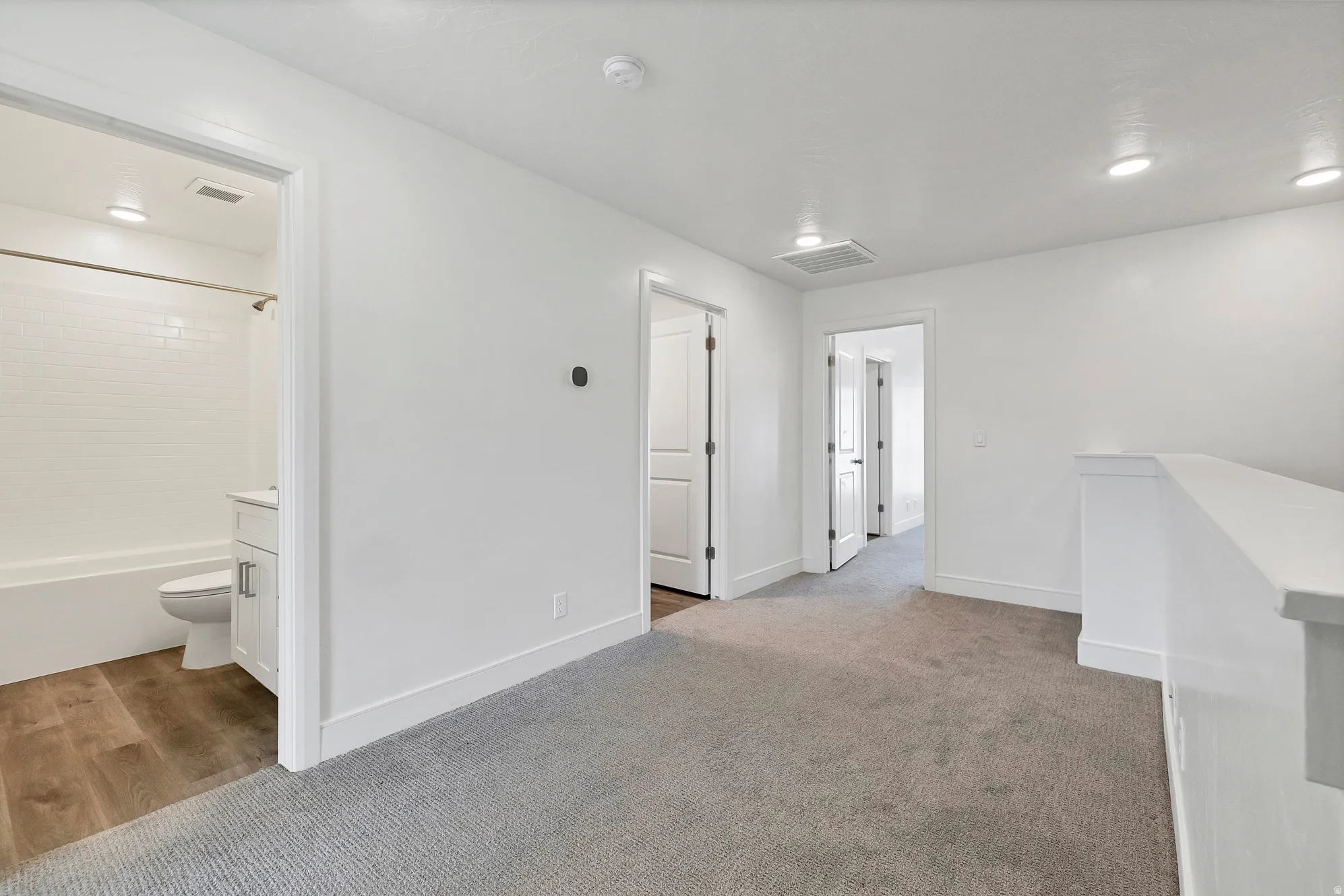 Upper-level landing featuring plush gray carpeting and a white railing system