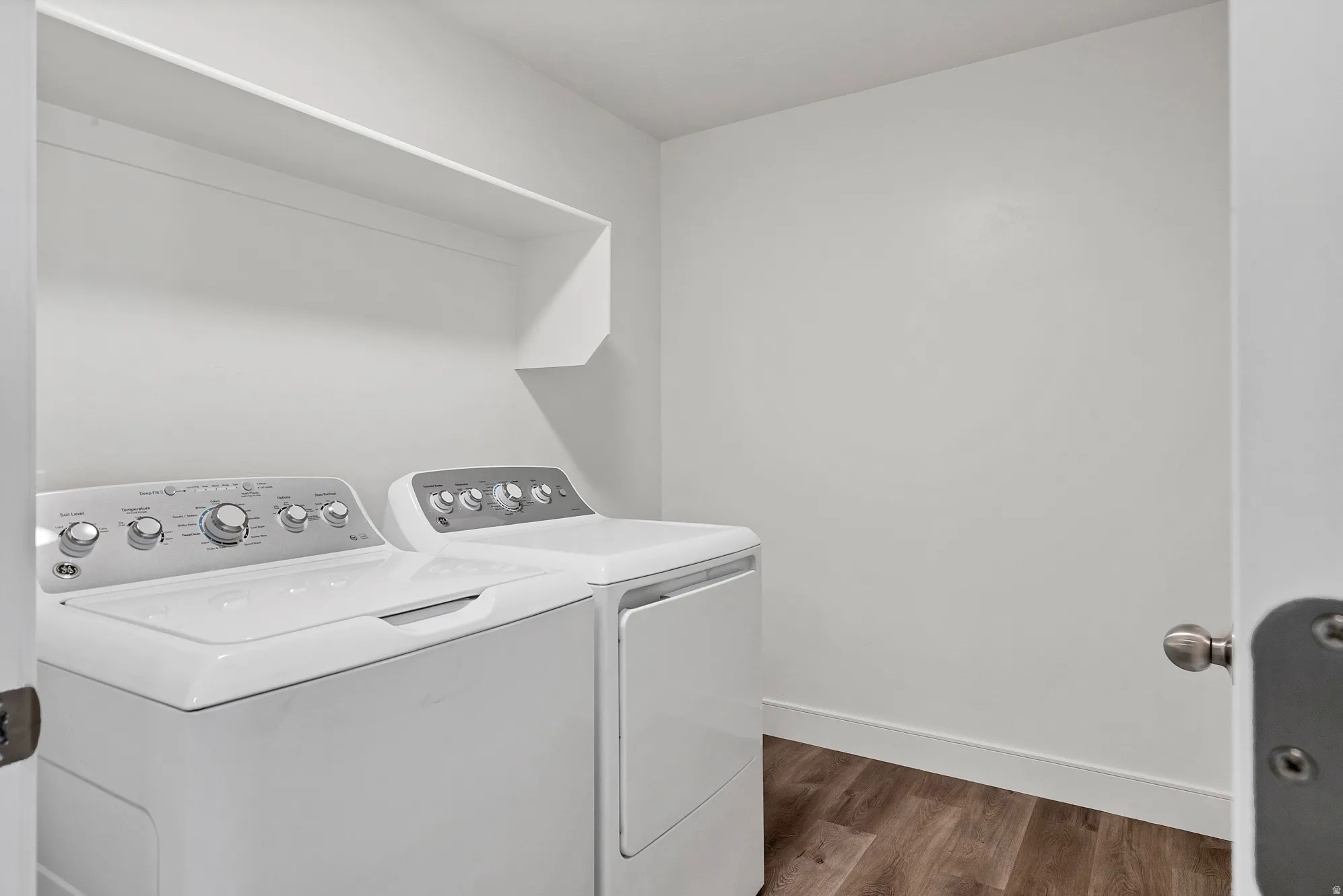 Dedicated laundry area featuring a washer and dryer, wood-finish flooring, white walls, and a built-in storage shelf