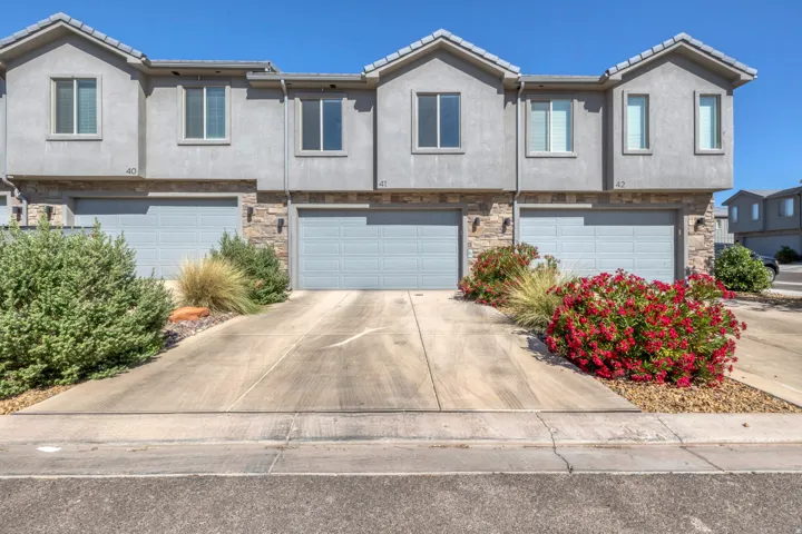 Stucco exterior townhome featuring stone accents and individual garage bays