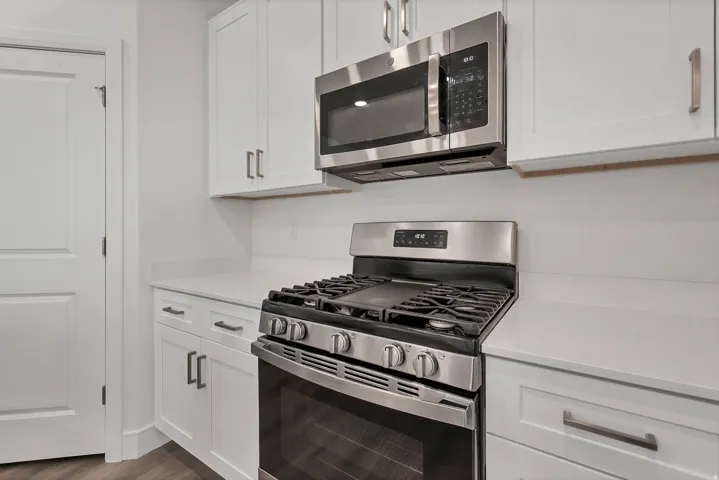 Modern kitchen featuring white shaker cabinetry, stainless steel gas range, stainless steel microwave, light-toned countertops, and wood-finish flooring