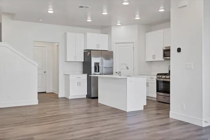 Open-concept kitchen featuring white cabinetry, stainless steel appliances, a central island with sink, and wood-finish flooring