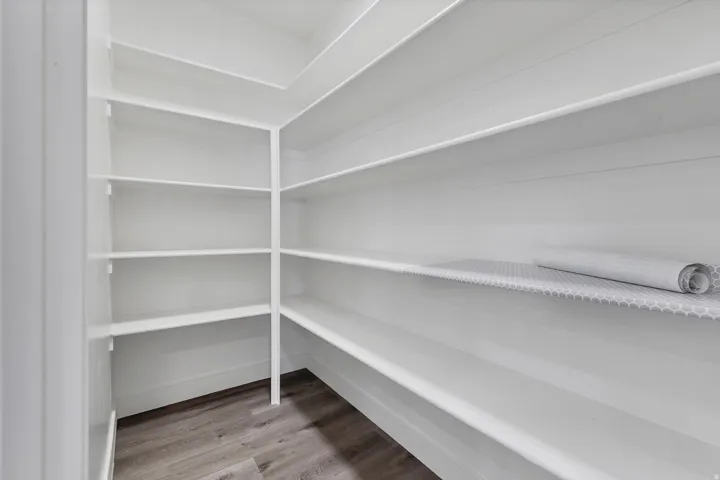Walk-in pantry featuring extensive white shelving and wood-finish flooring