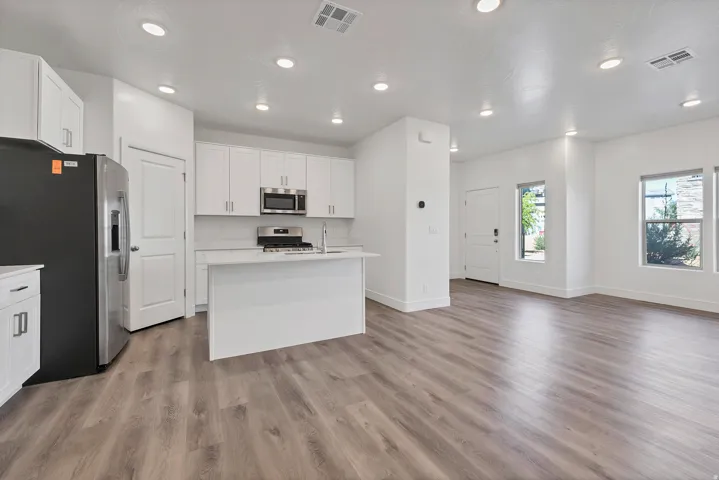 Open-concept living area featuring wood-finish flooring, recessed lighting, and a kitchen with white cabinetry, stainless steel appliances, and a central island with a sink