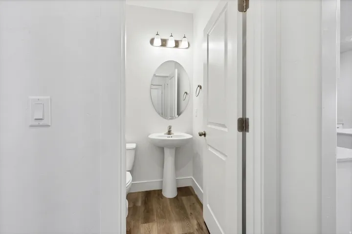 Compact bathroom featuring a white pedestal sink, oval mirror, and wood-finish flooring
