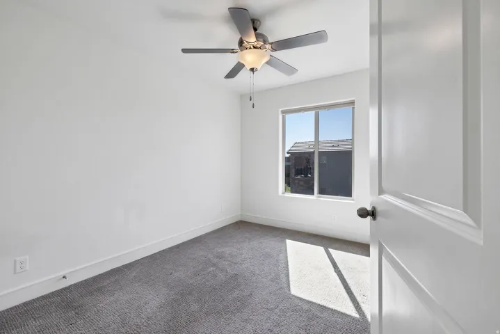 Carpeted room featuring a ceiling fan with integrated lighting, a window, and a white interior door with dark hardware