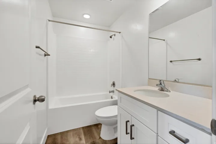 Bathroom featuring a white subway tile tub surround, wood-finish flooring, white vanity with stone-look countertop, and a large wall-mounted mirror