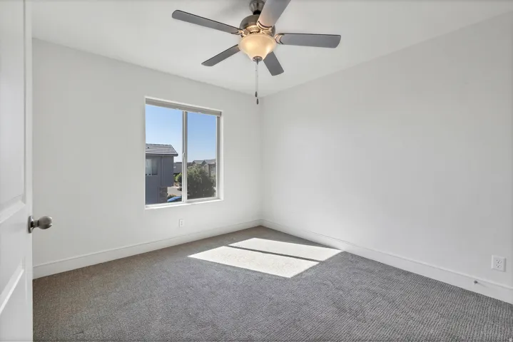 Neutral toned room featuring a single window, a ceiling fan with integrated lighting, white walls, gray carpeting, and white baseboards