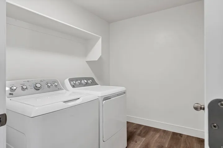 Dedicated laundry area featuring a washer and dryer, wood-finish flooring, white walls, and a built-in storage shelf