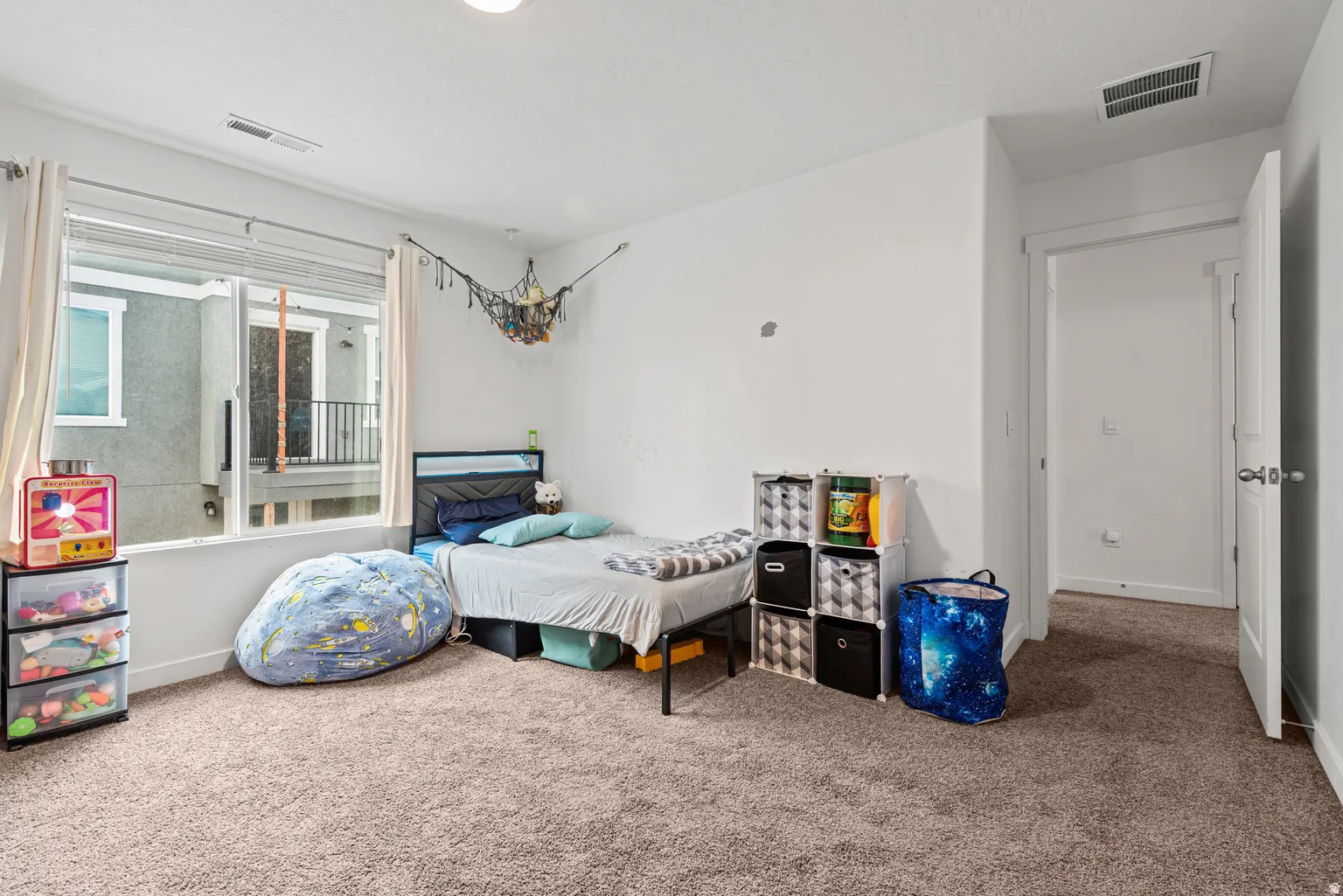 Bedroom featuring light tan carpeting, a large window with blinds and curtains, white walls, and white trim