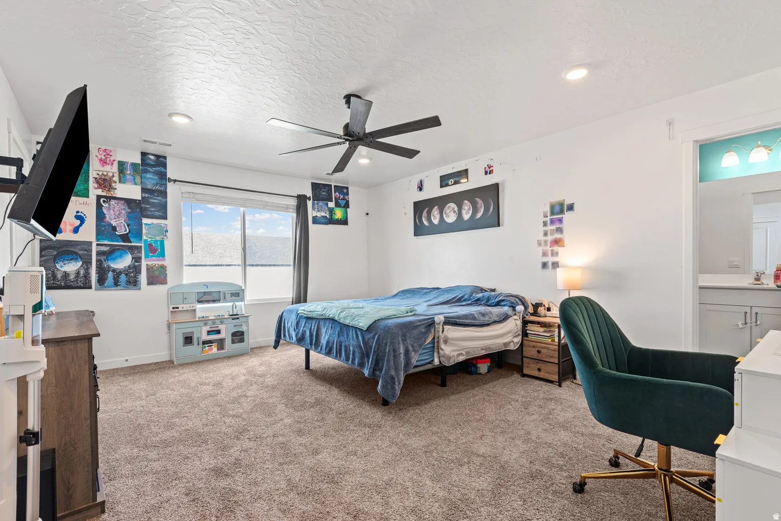 Spacious room featuring neutral carpet, a large window with roller shades, and a ceiling fan with integrated lighting