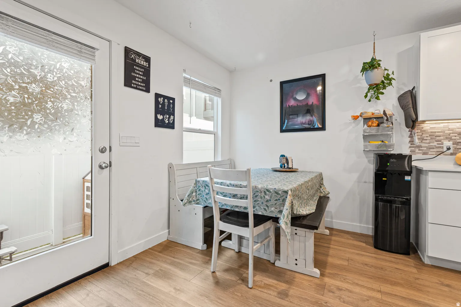 Kitchen dining area featuring wood-finish flooring, white cabinetry, and a patterned tile backsplash