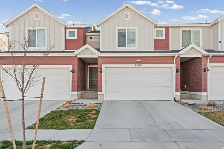 Contemporary townhouse exterior featuring red and beige siding, a prominent two-car garage, and a covered entryway