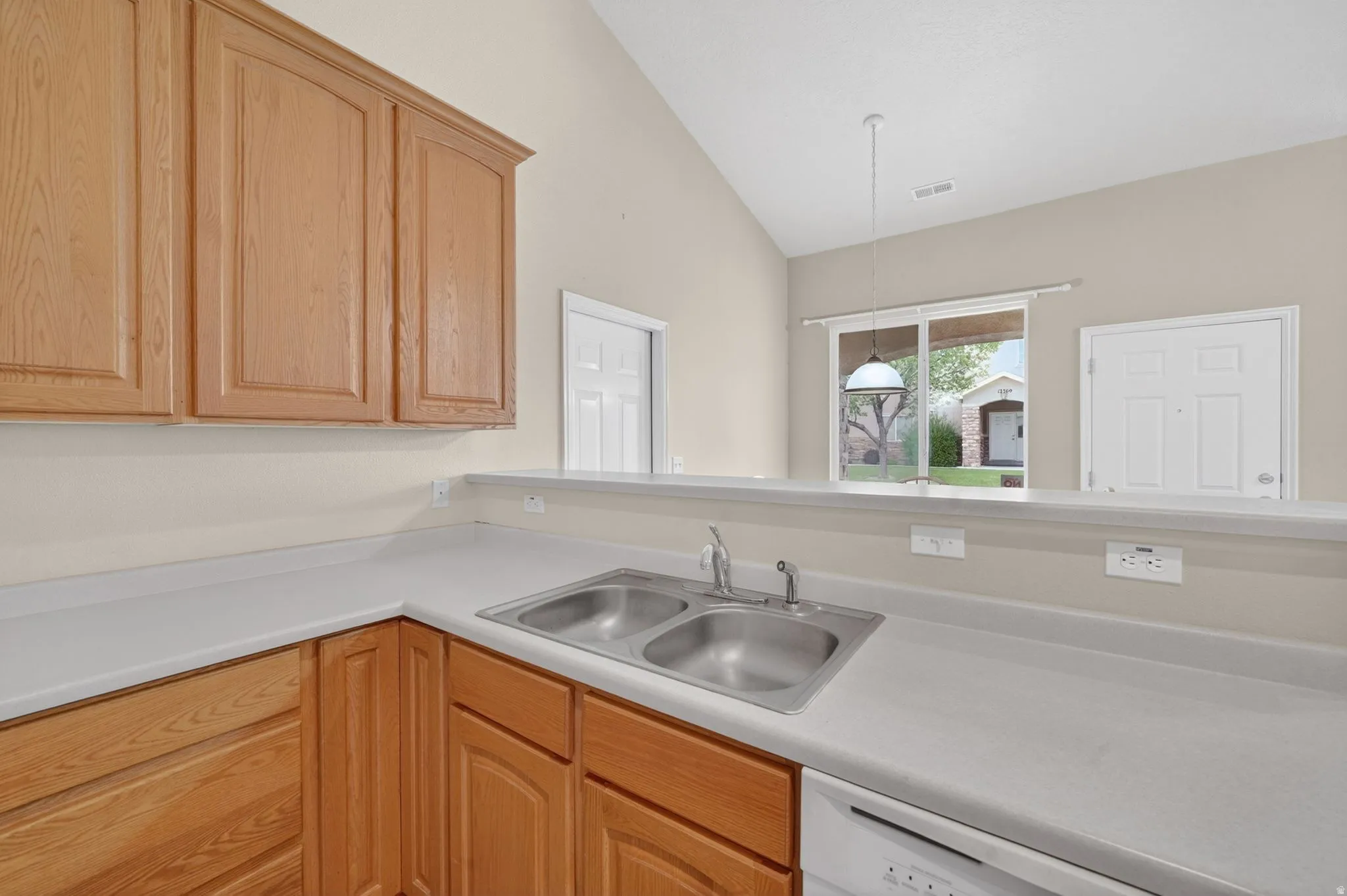 Kitchen featuring wood cabinetry, light countertops, dual basin stainless steel sink, and a white dishwasher