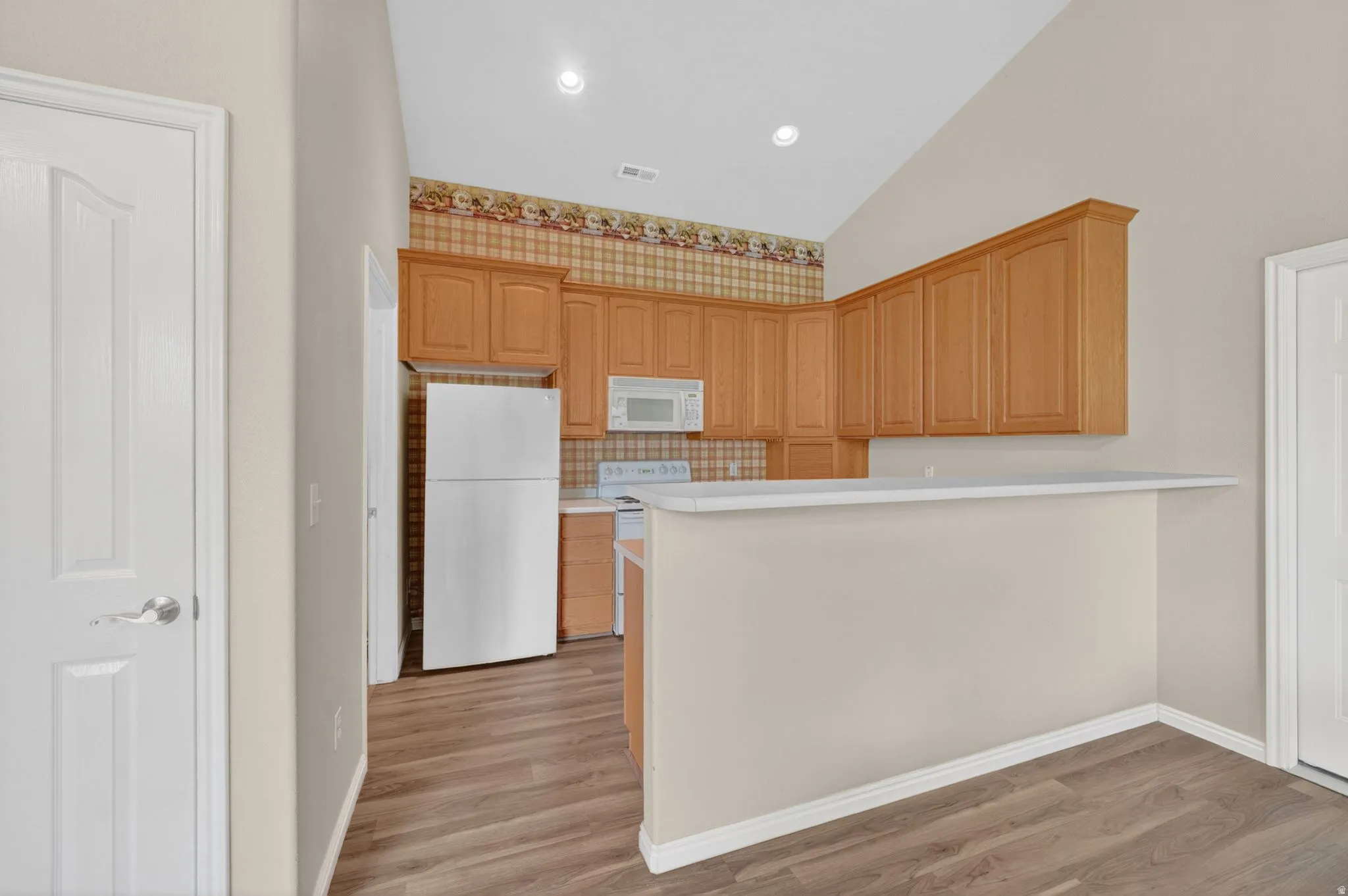 Kitchen featuring wood-finish flooring, vaulted ceiling, recessed lighting, wood cabinetry, and a breakfast bar