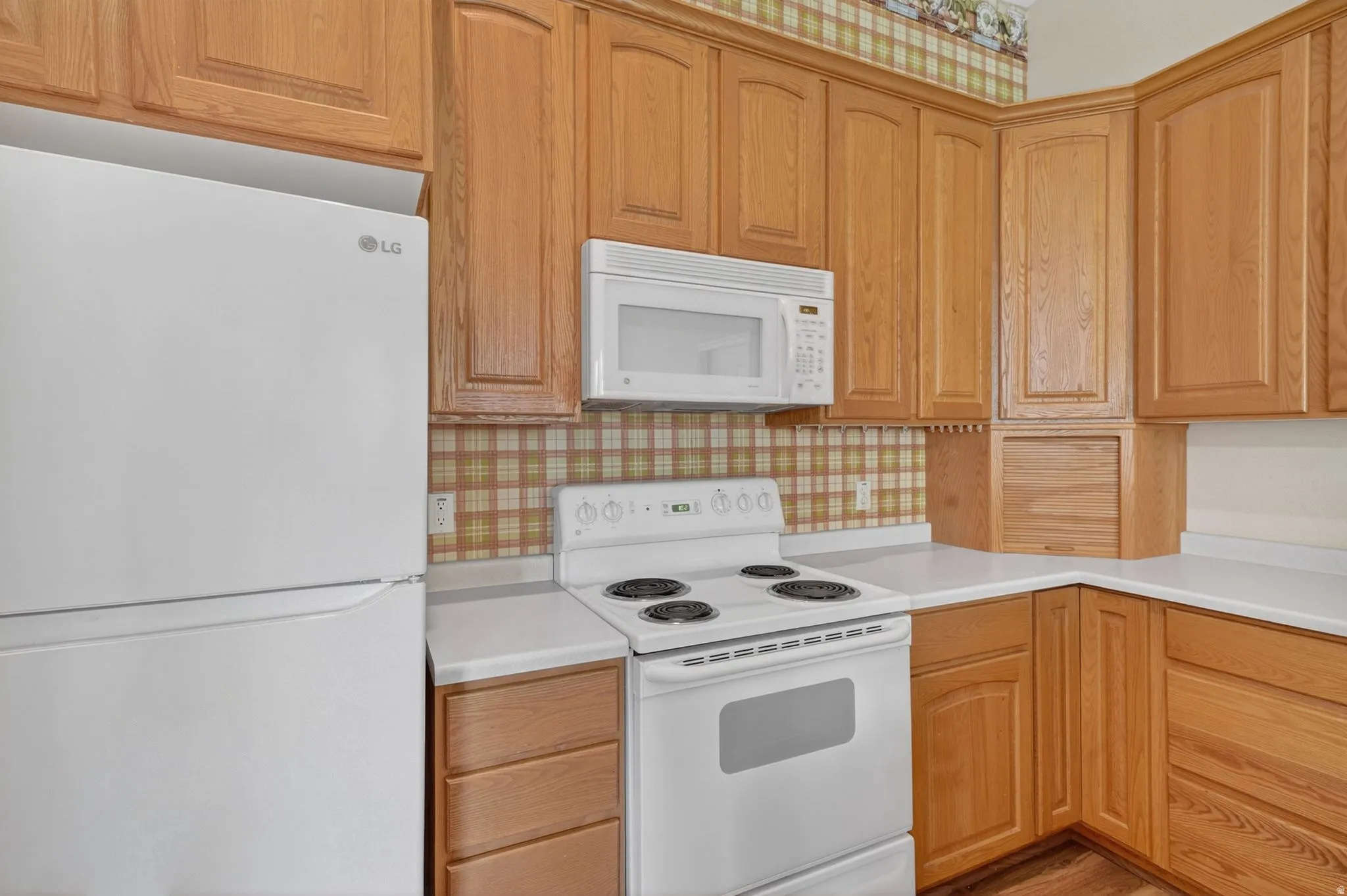 Kitchen featuring white appliances, wood cabinetry, light-toned countertops, and a patterned backsplash