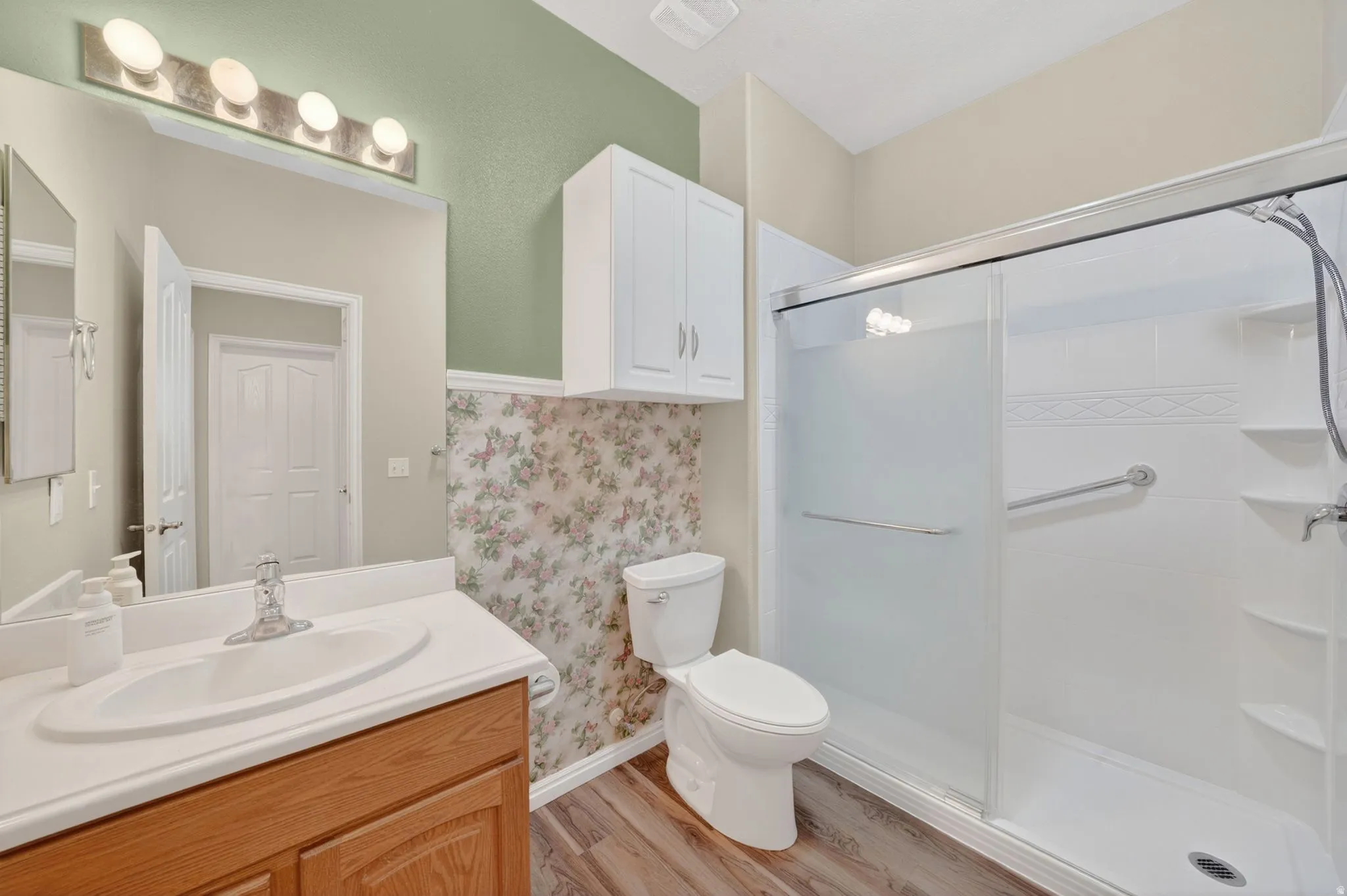 Bathroom featuring a wood-finish vanity with an integrated sink, a large wall mirror, and a four-bulb vanity light fixture