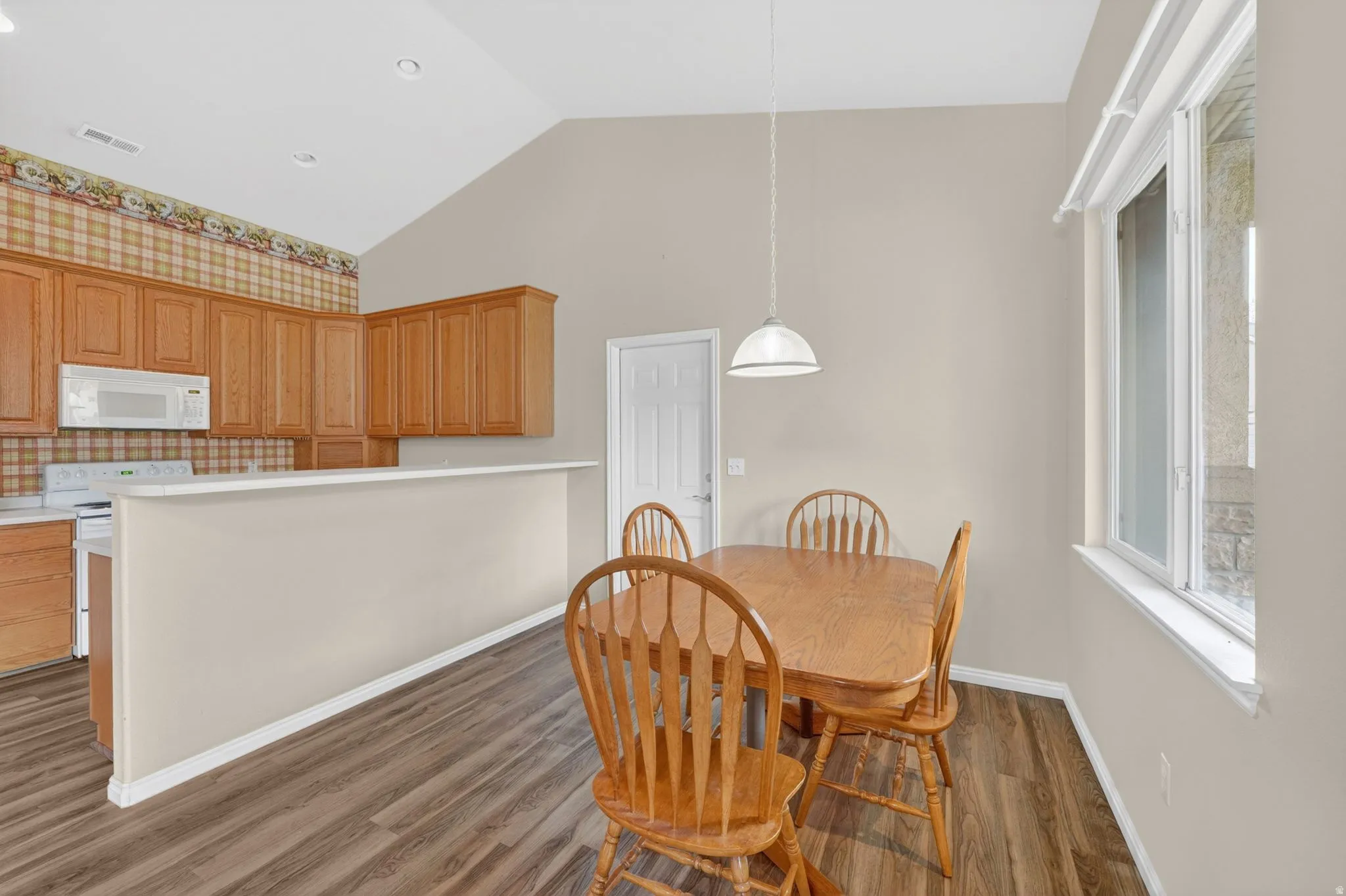 Open-concept kitchen and dining area featuring wood-finish flooring, vaulted ceilings, and natural wood cabinetry
