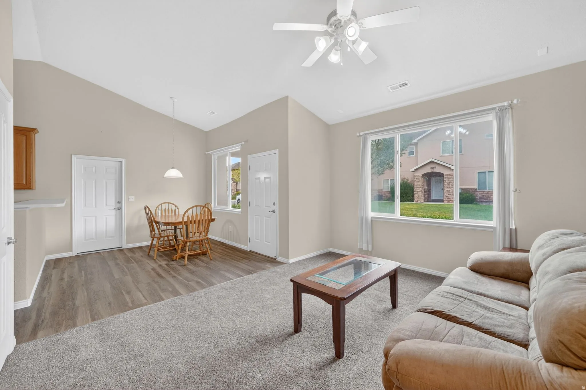 Open-concept living space featuring vaulted ceilings, wood-finish flooring, and a ceiling fan with light fixture