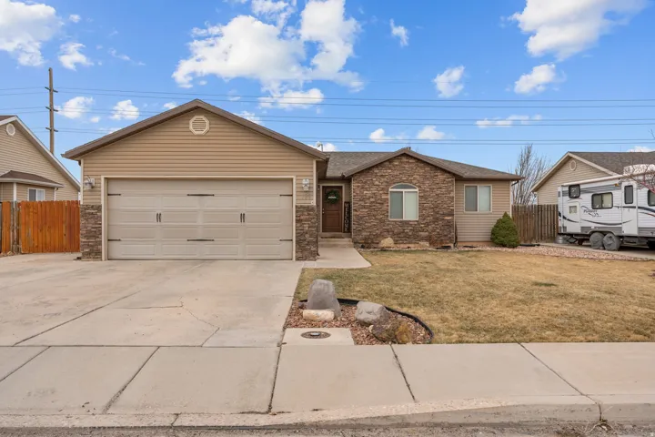 Ranch-style exterior featuring a two-car garage, stone facade accents, light beige siding, and a concrete driveway