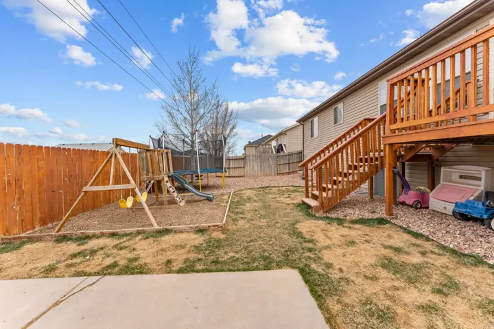 Fenced backyard featuring a wooden privacy fence, a multi-level wooden deck with stairs, a concrete patio, and a play structure