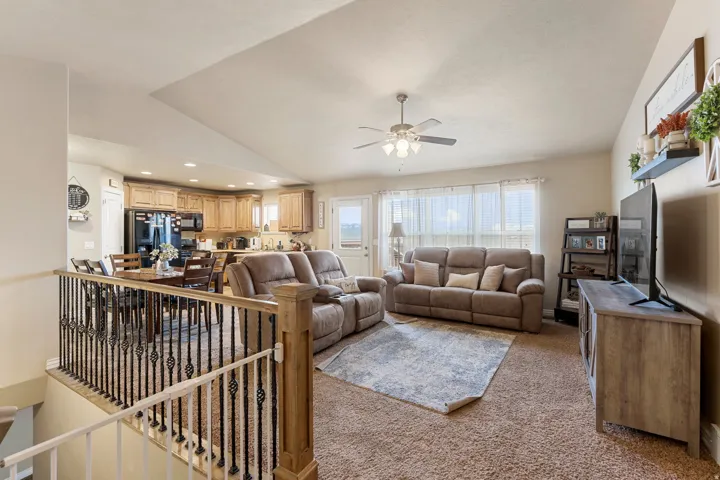 Open-concept living space with vaulted ceilings, natural wood cabinetry, black appliances, and a ceiling fan with integrated lighting