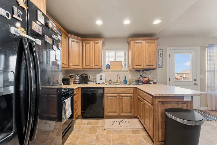 U-shaped kitchen featuring wood cabinetry, light-toned countertops, tile flooring, and integrated black appliances