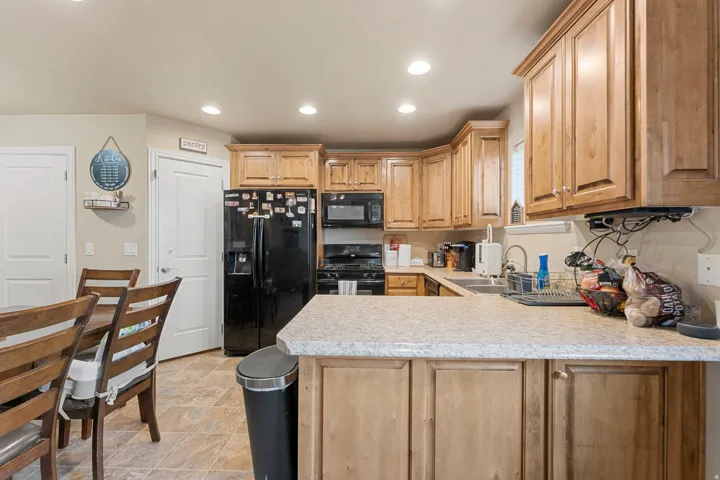 Open-concept kitchen featuring light wood cabinetry, black appliances, a double basin sink, recessed lighting, and a peninsula with a light-toned countertop