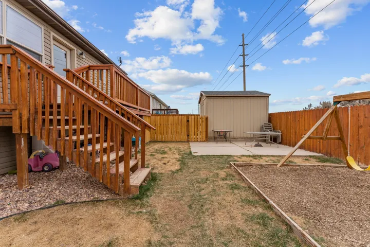 Expansive backyard featuring a multi-level wooden deck with stairs, a privacy fence, a detached storage shed, a concrete patio, and a dedicated play area with wood chips