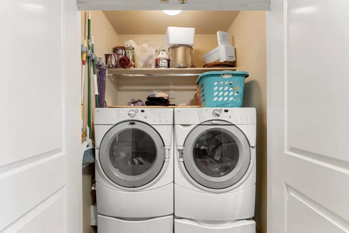 Dedicated laundry area featuring dual front-loading appliances, a wood-finish countertop, and built-in shelving