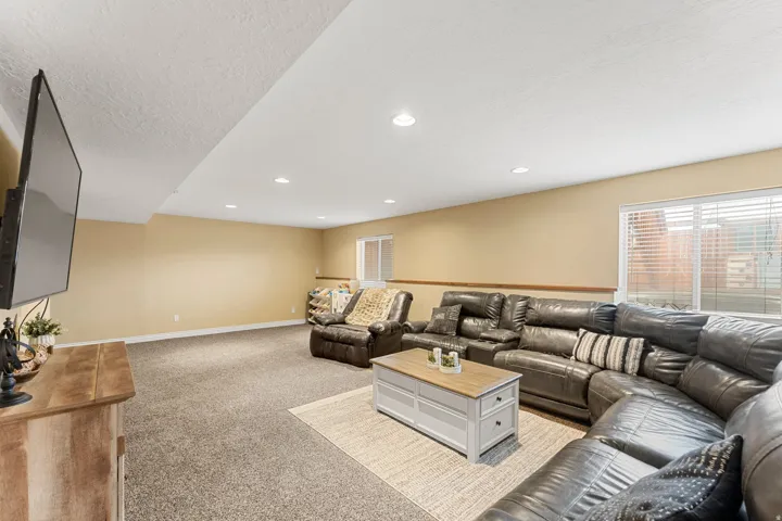 Spacious living area featuring neutral-toned carpeting, recessed lighting, and a wood-finish media console