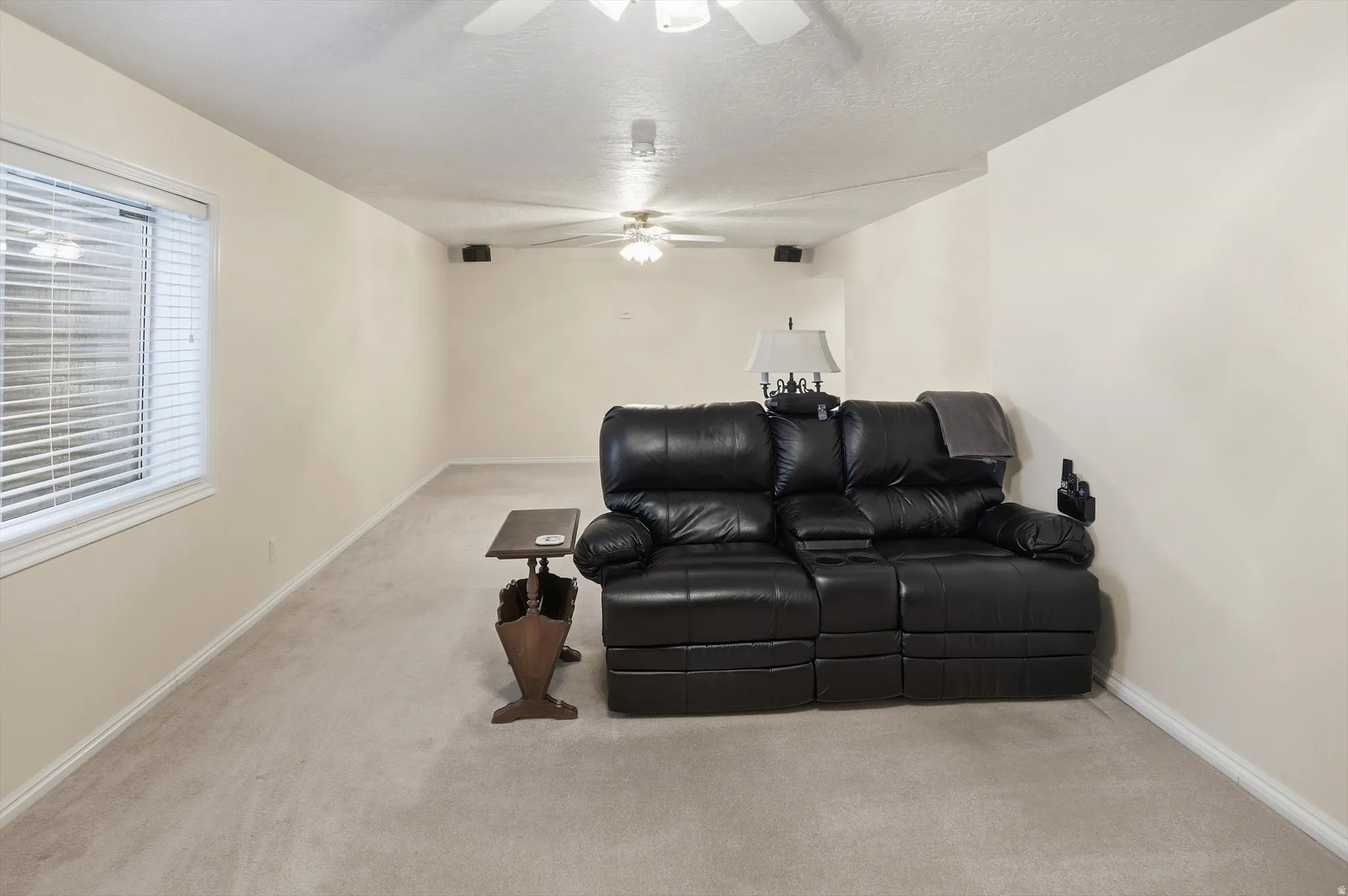 Spacious room featuring neutral carpeting, light-toned walls, and a window with horizontal blinds