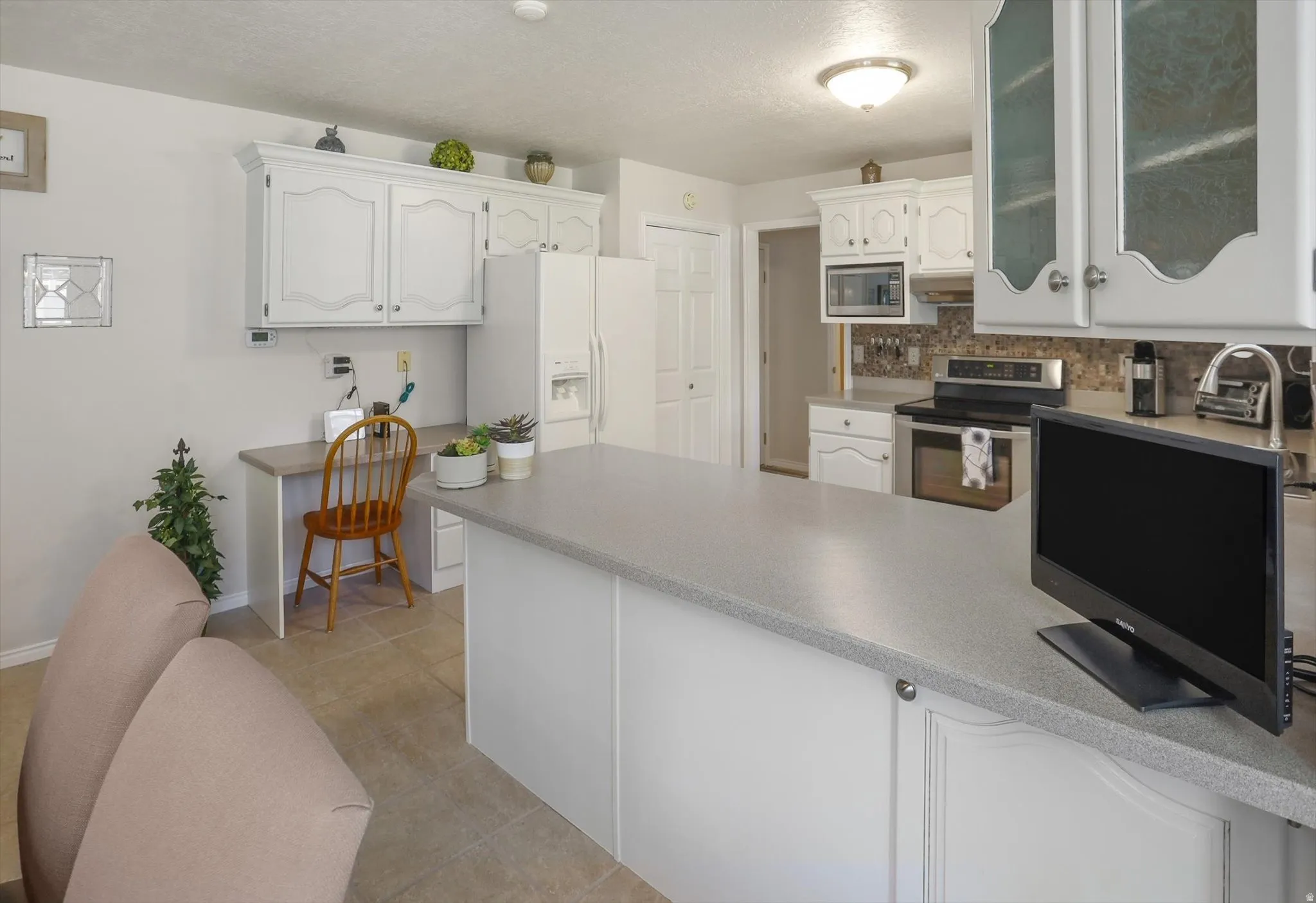 Kitchen featuring white cabinetry with decorative molding, a built-in desk area, white appliances, and a mosaic tile backsplash