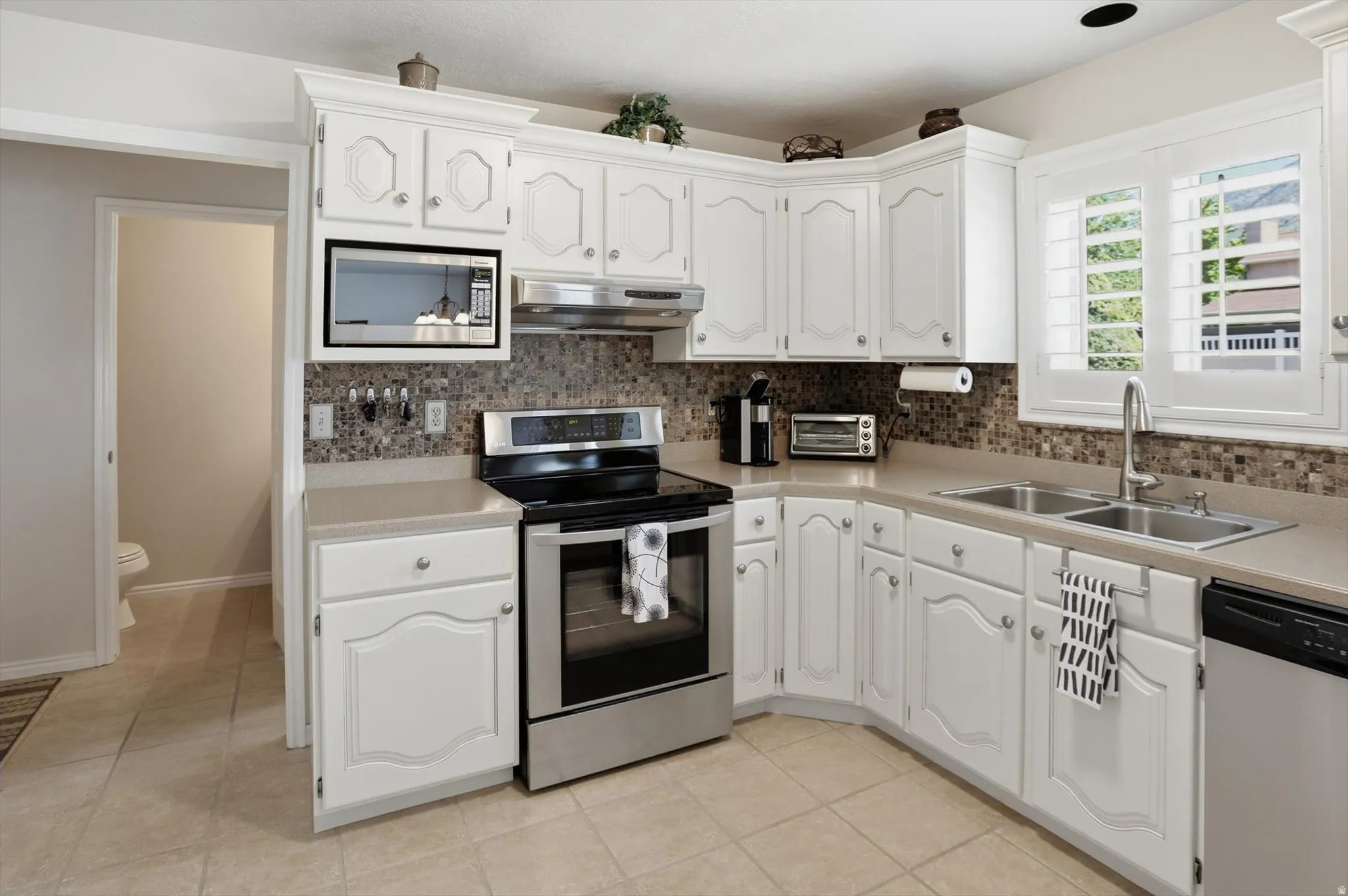 Kitchen featuring white cabinetry, light-toned countertops, a mosaic tile backsplash, and stainless steel appliances