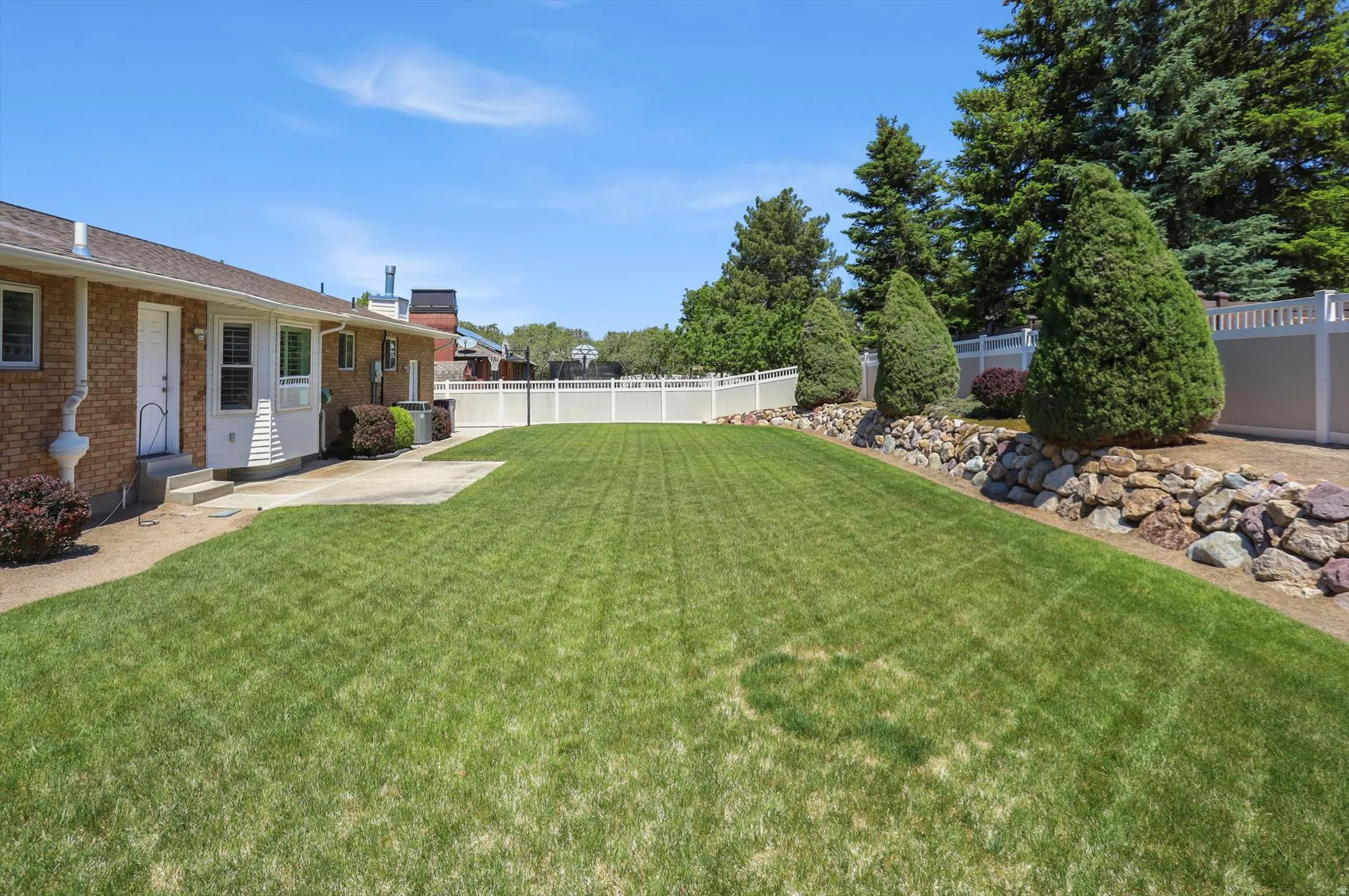 Expansive lawn area featuring a concrete patio, brick exterior, and a white privacy fence