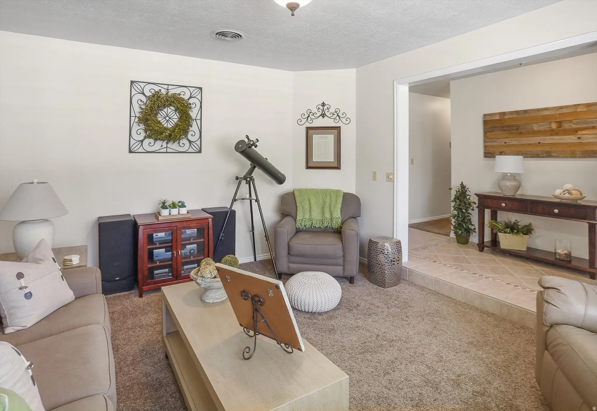 Spacious living area featuring neutral-toned walls, plush carpet flooring, and an open doorway to a tiled entry