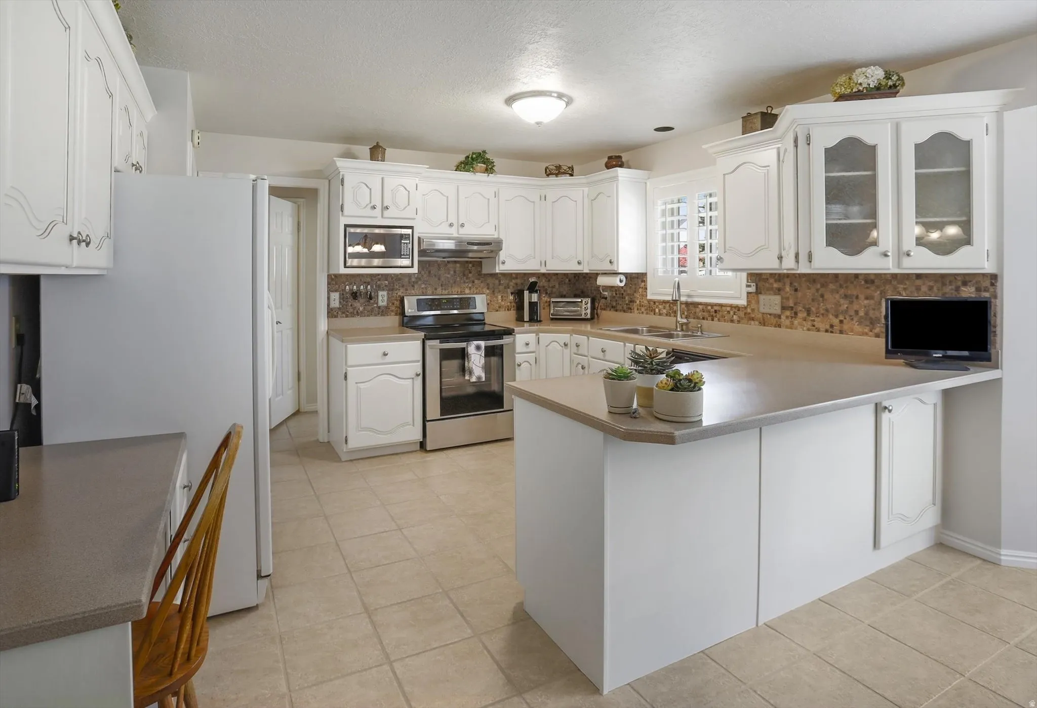 Expansive kitchen featuring white cabinetry, a tiled backsplash, stainless steel appliances, and a central island with a built-in counter extension