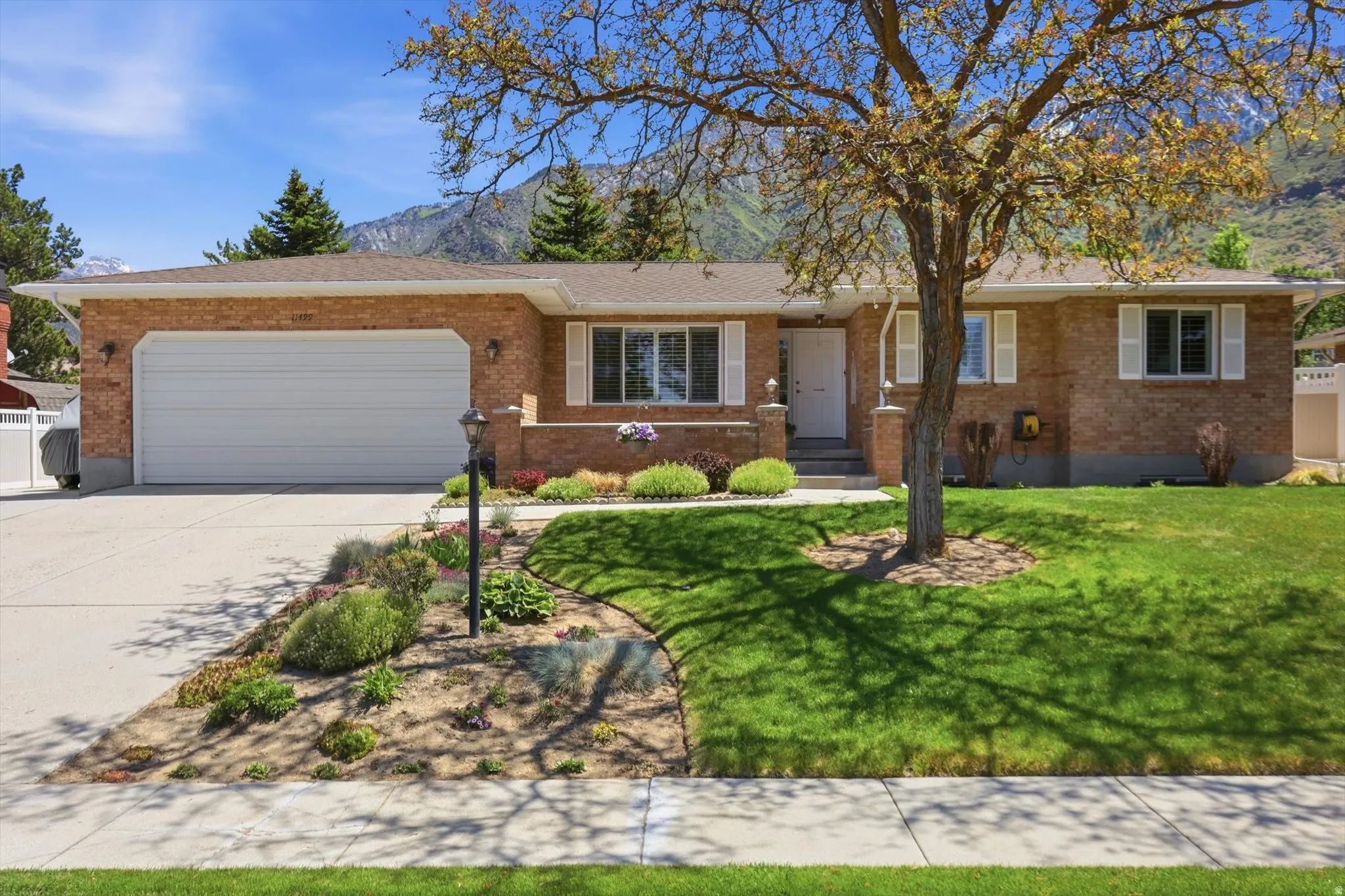 Brick exterior with a white garage door, concrete driveway, and established landscaping