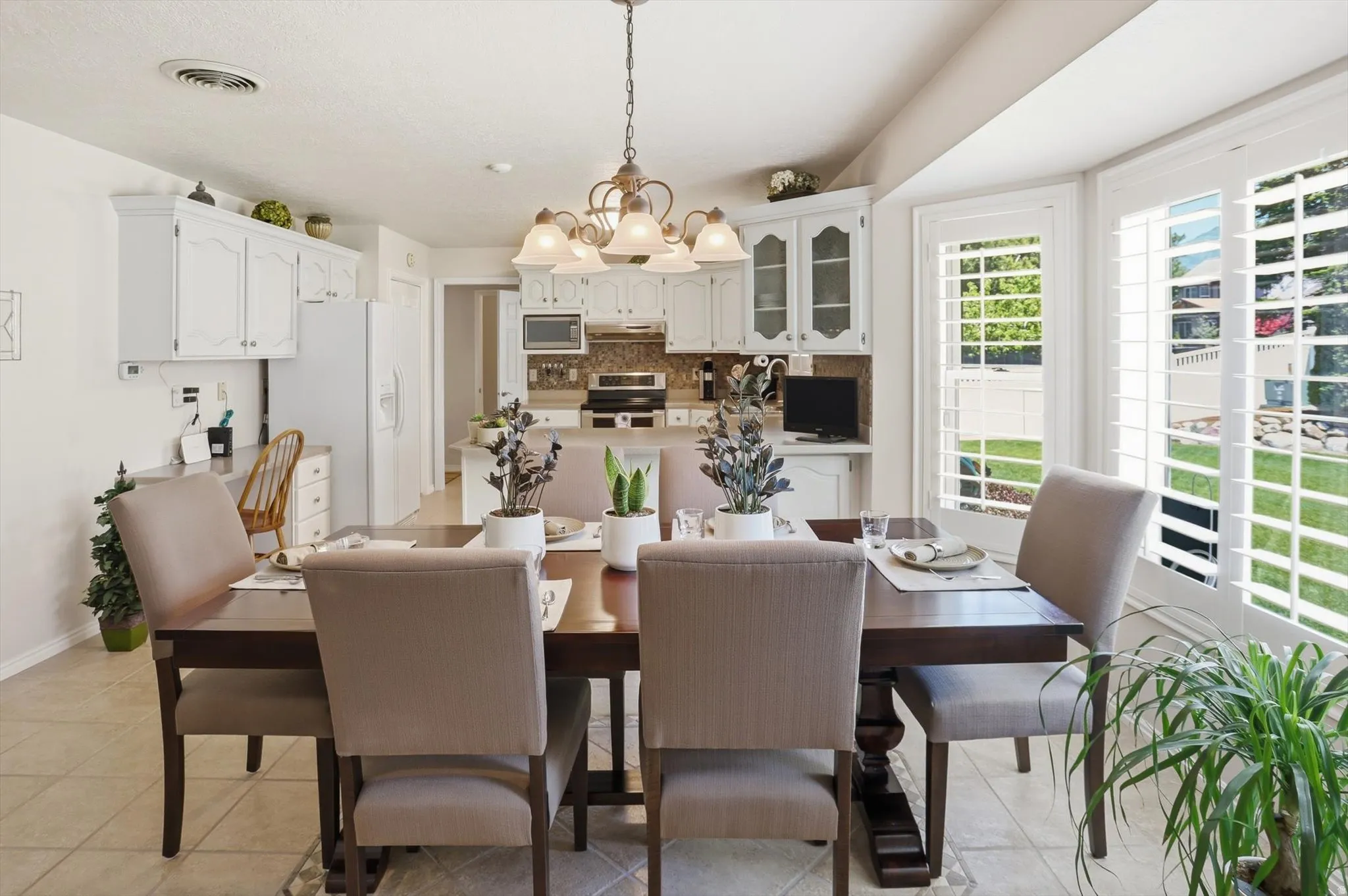 Dining area featuring an ornate chandelier, tile flooring, and plantation shutters