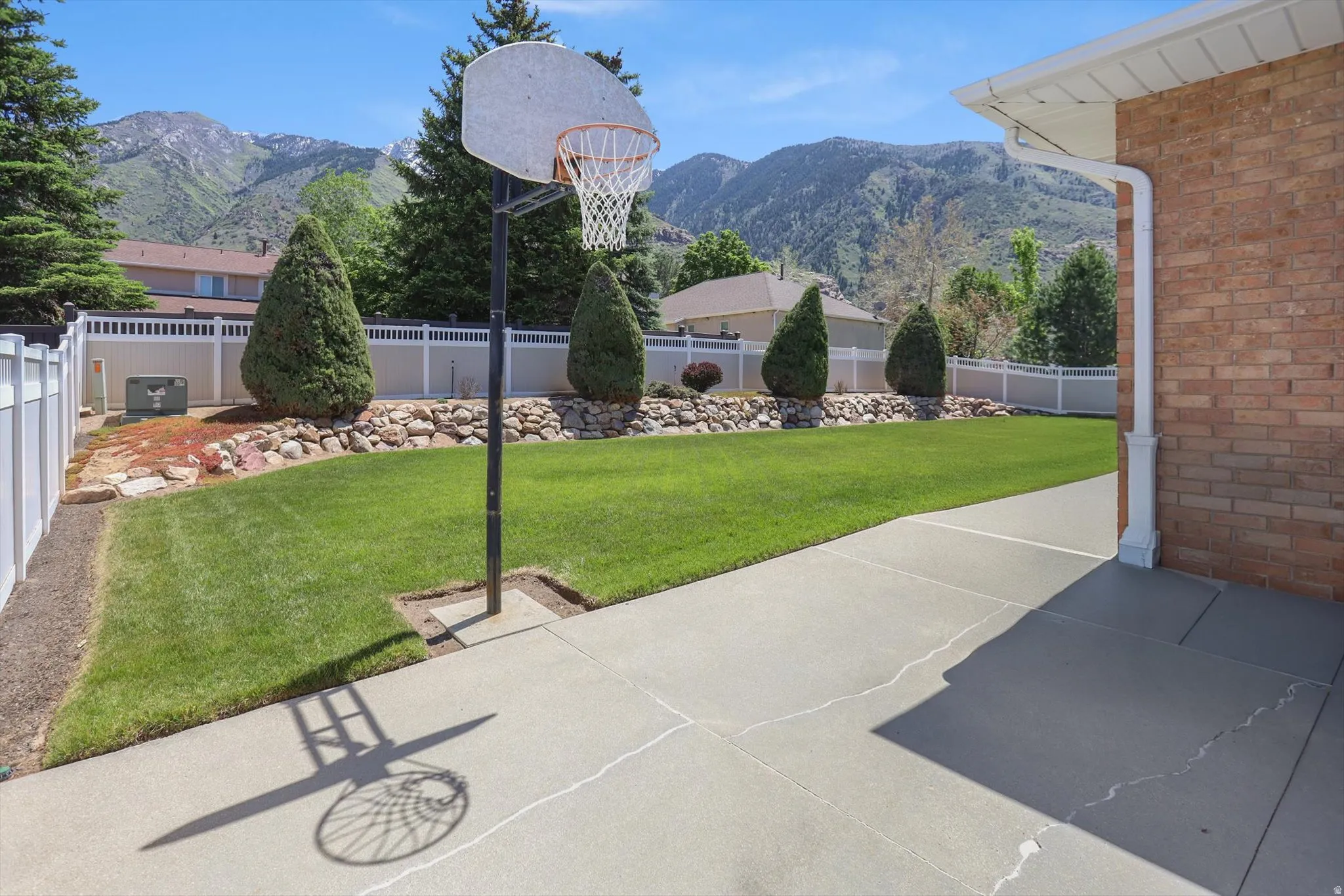 Spacious backyard featuring a basketball hoop, expansive lawn, and mature trees