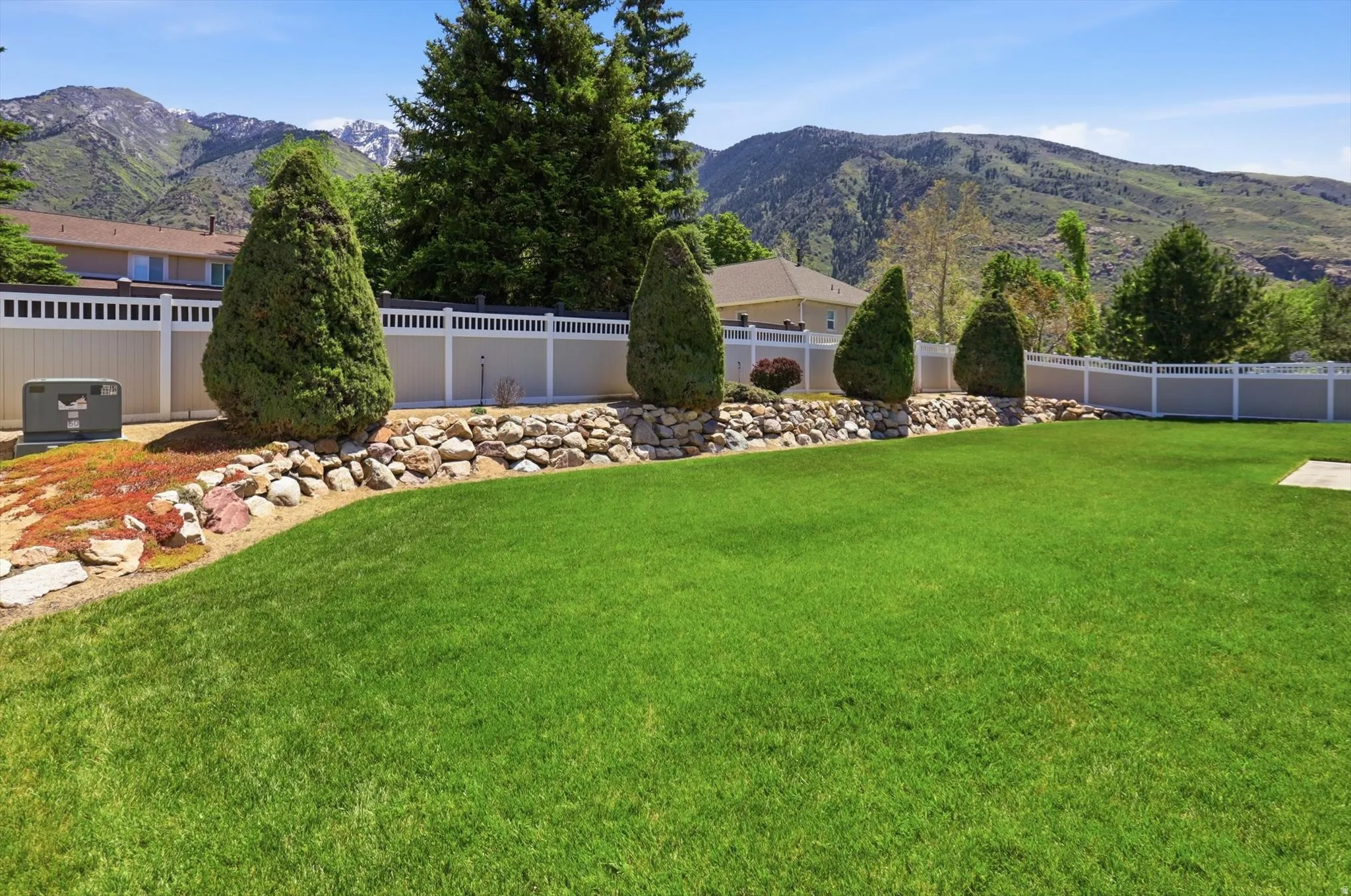 Expansive green lawn with a rock retaining wall and established conical evergreens