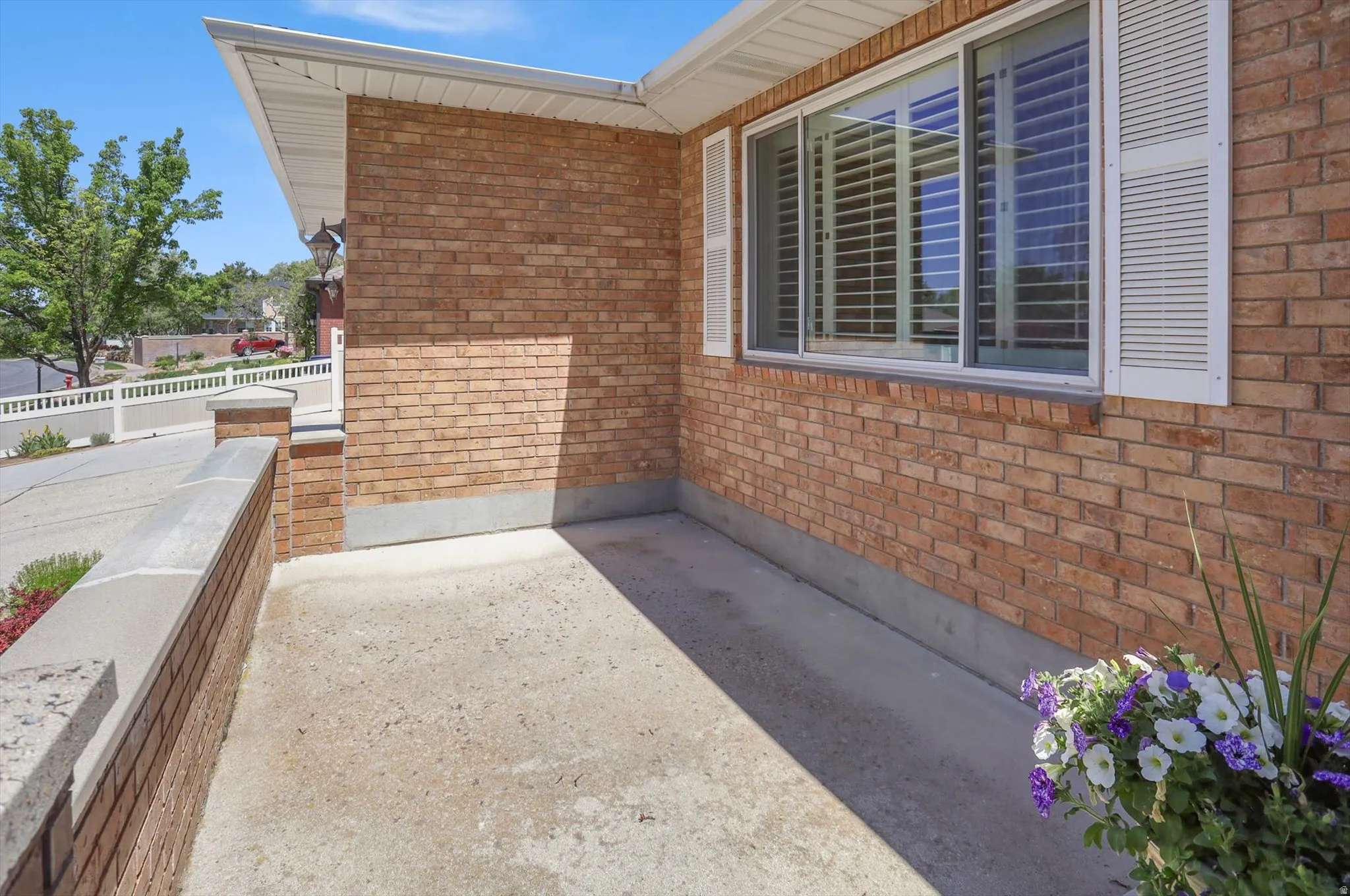 Brick exterior featuring a window with white shutters, an overhang with soffit, and a low brick wall with a stone cap