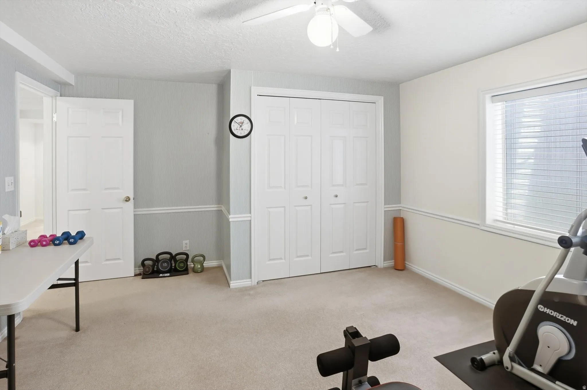 Carpeted room featuring a white ceiling fan with light fixture, light-toned walls with chair rail molding, and a window with horizontal blinds