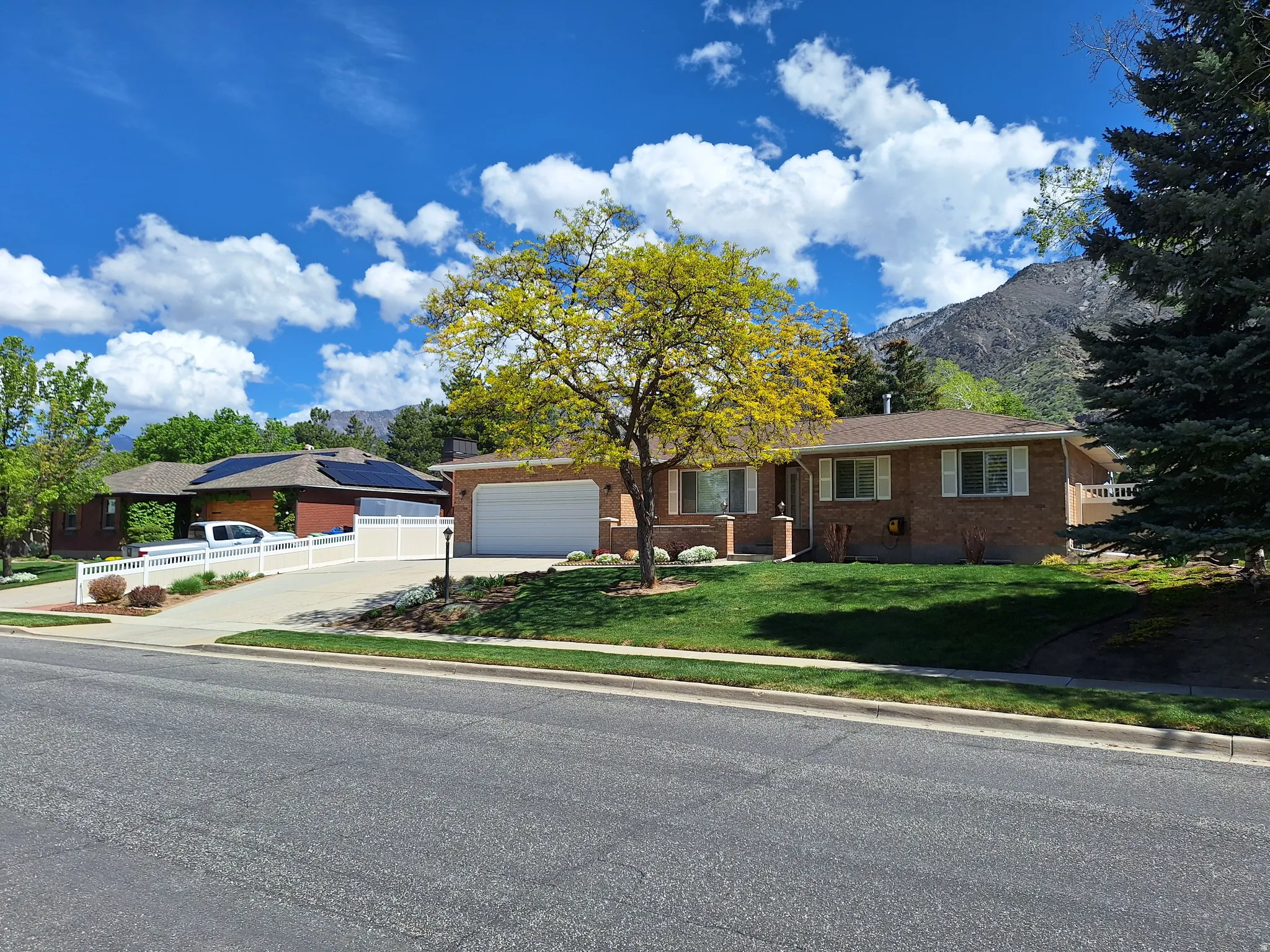 Brick exterior residence with an attached garage, featuring a verdant front lawn and mature landscaping