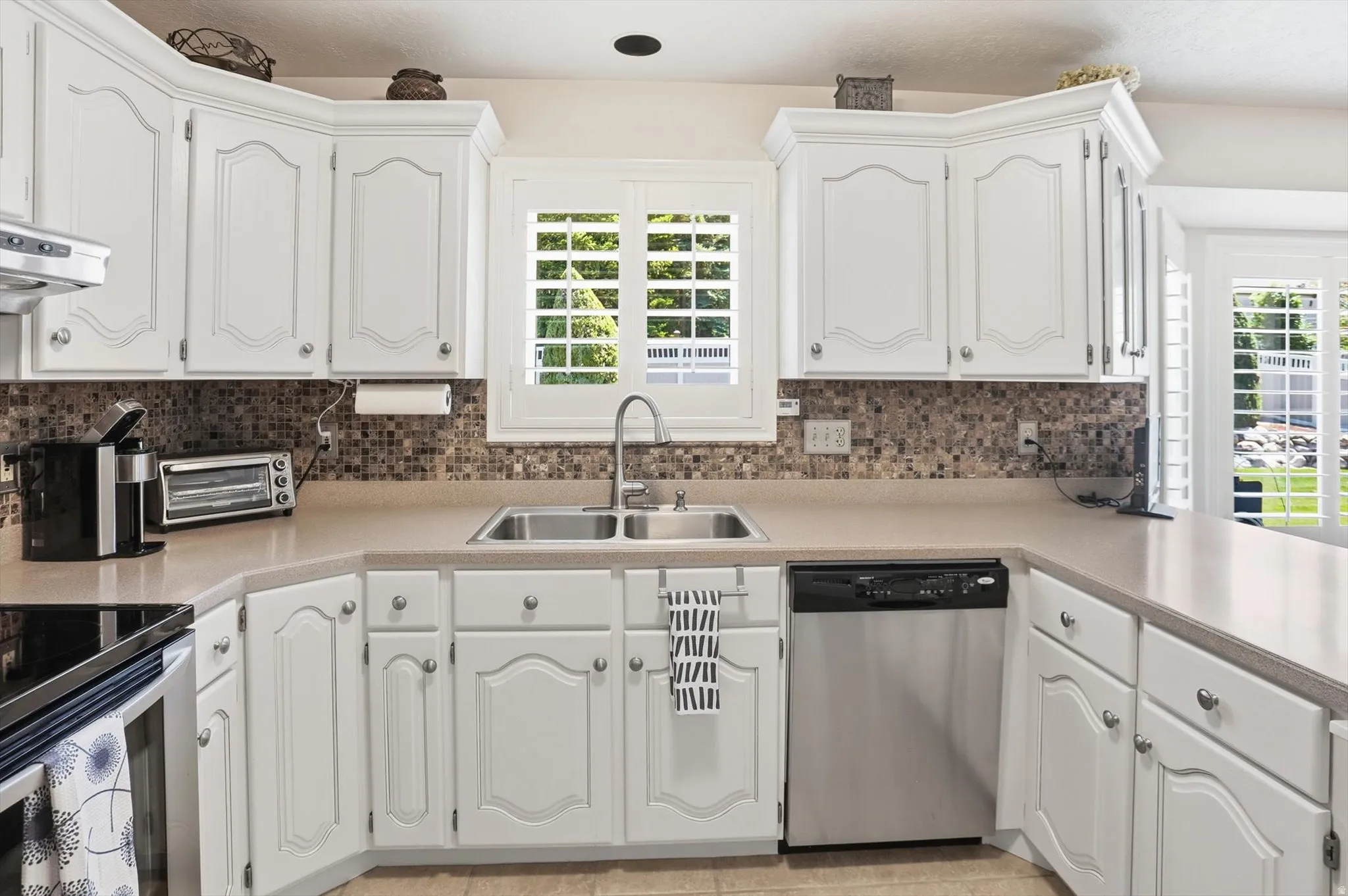 U-shaped kitchen featuring white cabinetry, a dual basin stainless steel sink with a high-arc faucet, and a mosaic tile backsplash